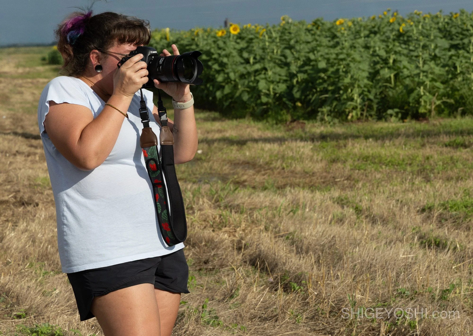A woman photographing a sunflower field with a Canon camera and floral camera strap