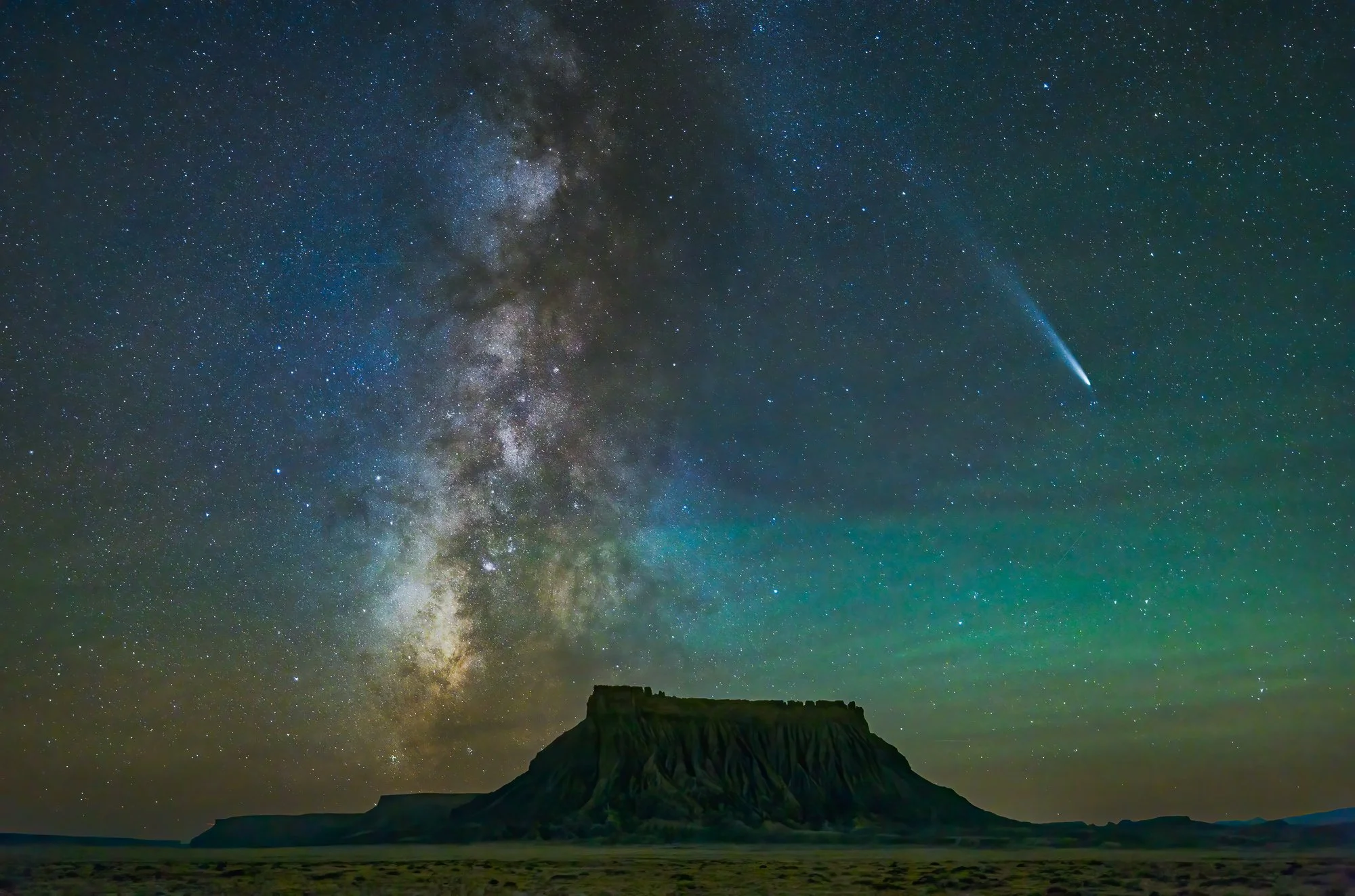 Factory Butte silhouetted against the Milky Way galaxy with Comet Tsuchinshan-ATLAS streaking across the night sky in Utah