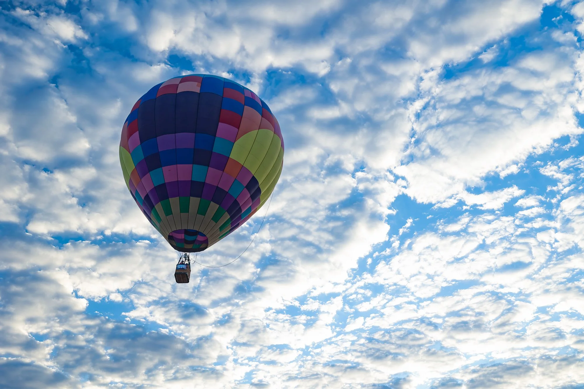Colorful hot air balloon floating against a dramatic blue sky filled with white clouds at the Albuquerque International Balloon Fiesta in New Mexico