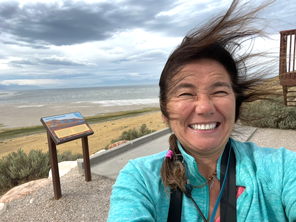 Woman smiling with wind-blown hair at scenic overlook near lake shore.