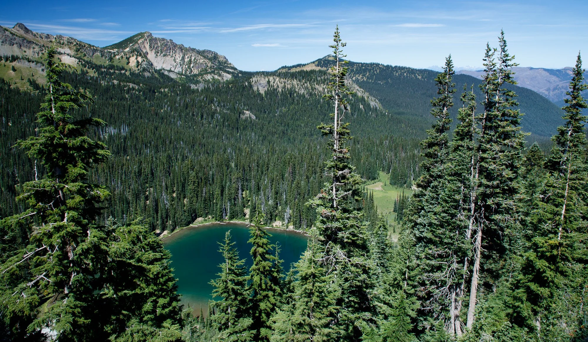 A turquoise alpine lake nestled among dense evergreen forest with rocky mountain peaks rising above in the Pacific Northwest.