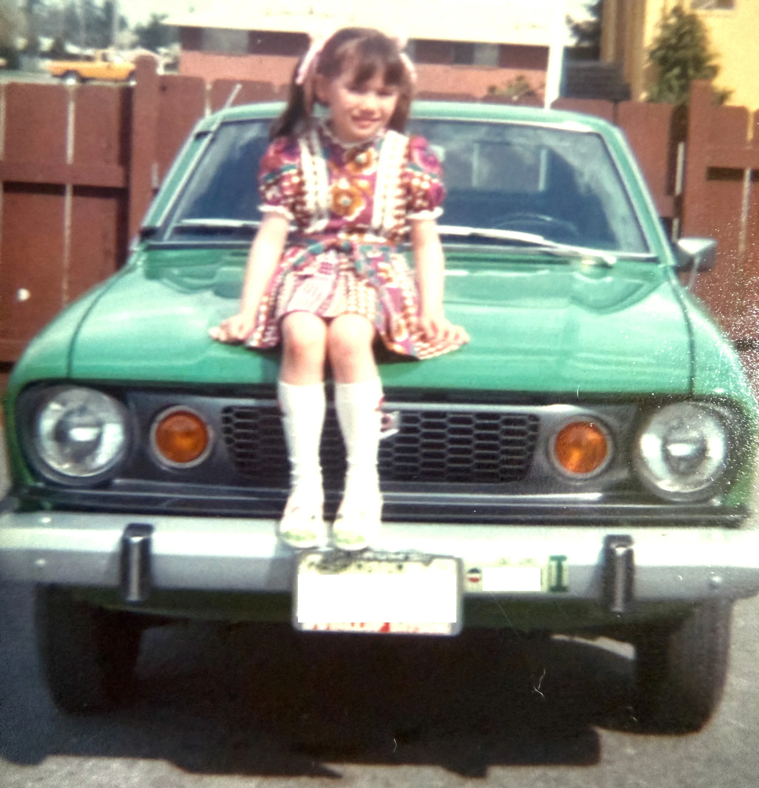 Young girl sitting on hood of green Datsun B210.