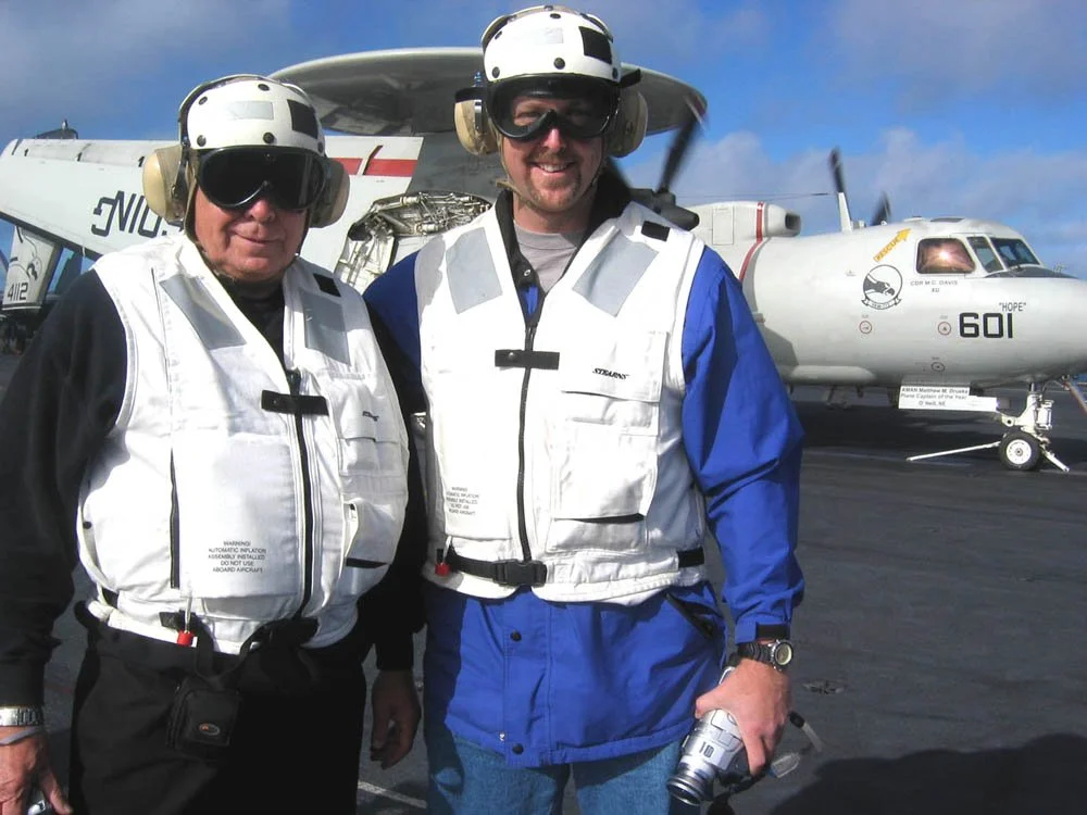 Two men in pilot gear standing on an aircraft carrier tarmac with a white military fighter jet in the background. Mapping, topographic maps, GIS, LiDAR, aerial mapping, SoCal, Southern California, aerial mapping, aerial imagery