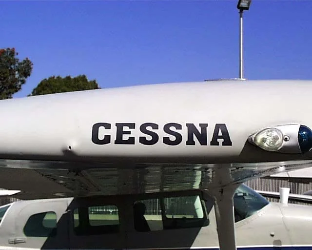Front view of a white CESSNA 206, for aerial mapping, aircraft parked outdoors with a clear blue sky and trees in the background. Mapping, topographic maps, GIS, LiDAR, aerial mapping, SoCal, Southern California, aerial mapping, aerial imagery