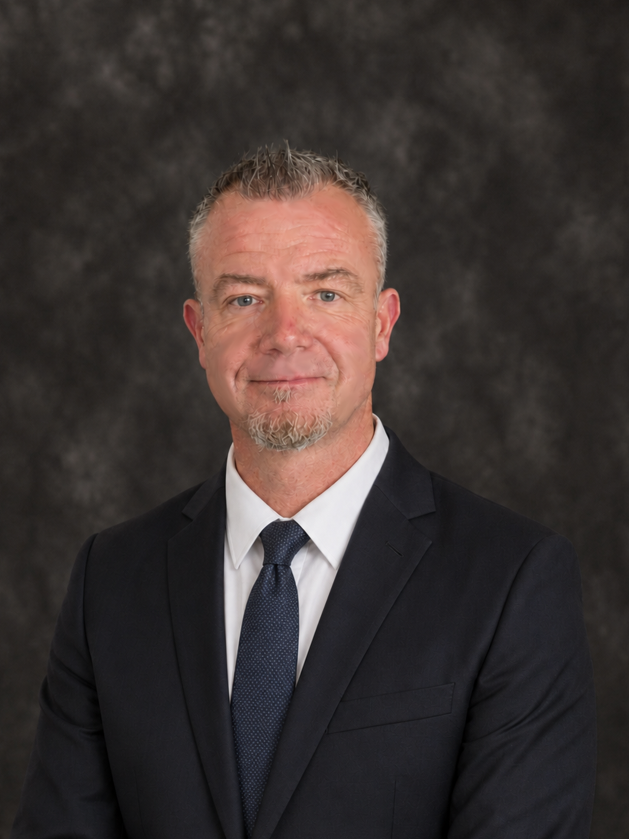 Mike McCarthy, project and operations manager at RJL & Associates, in a black suit, white shirt, and dark tie, smiling in a headshot against a dark, textured background.