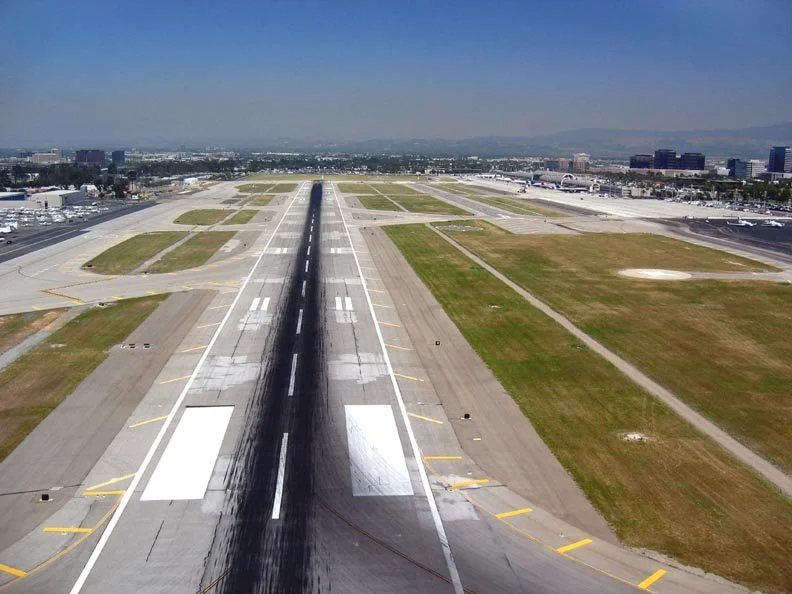 Aerial view of John Wayne's runway with tire marks and taxiways on either side, spanning towards Irvine and Newport's city skyline in the distance. Mapping, topographic maps, GIS, LiDAR, aerial mapping, SoCal, Southern California, aerial mapping,
