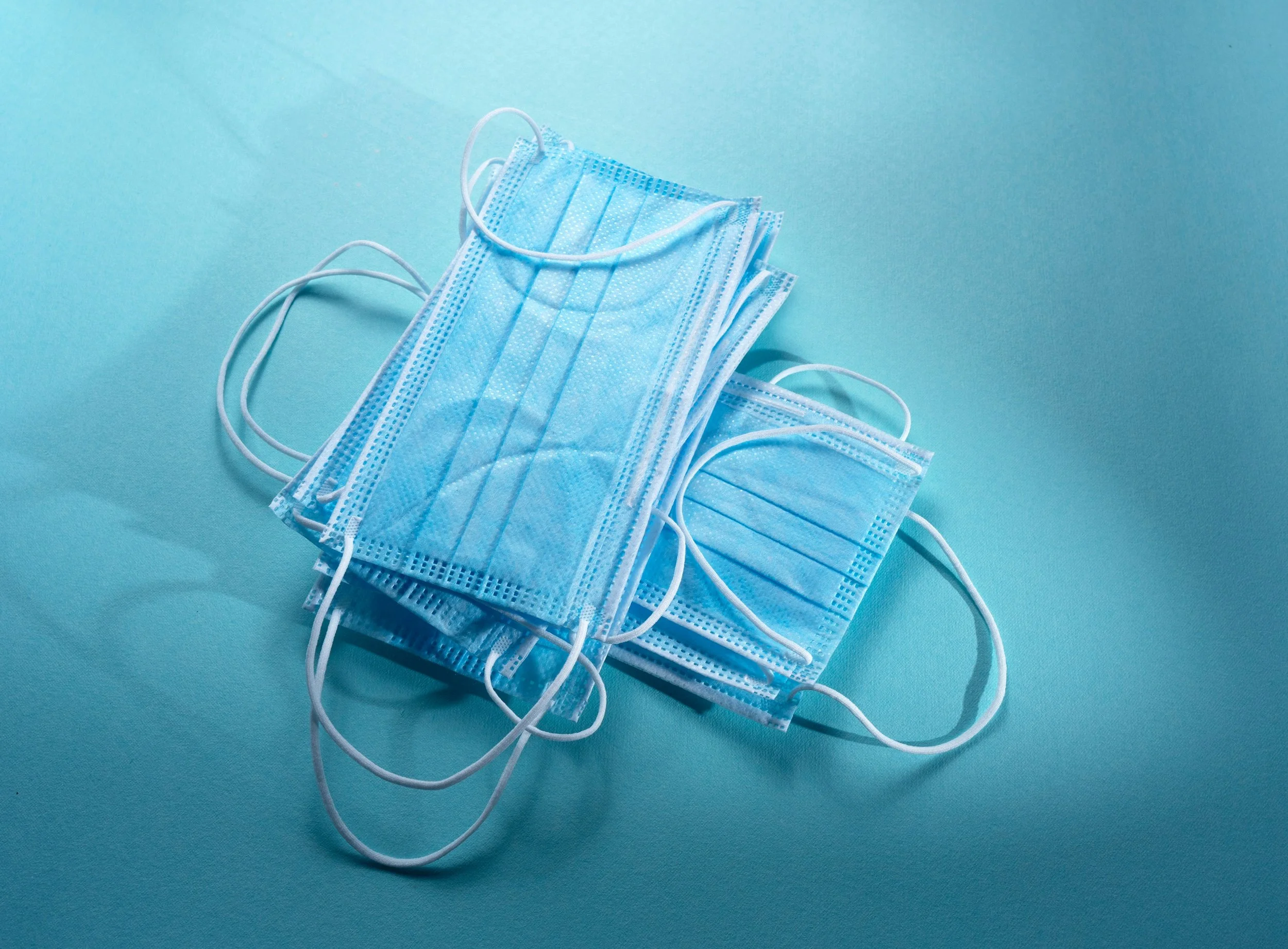 A stack of disposable blue surgical masks on a light blue background.