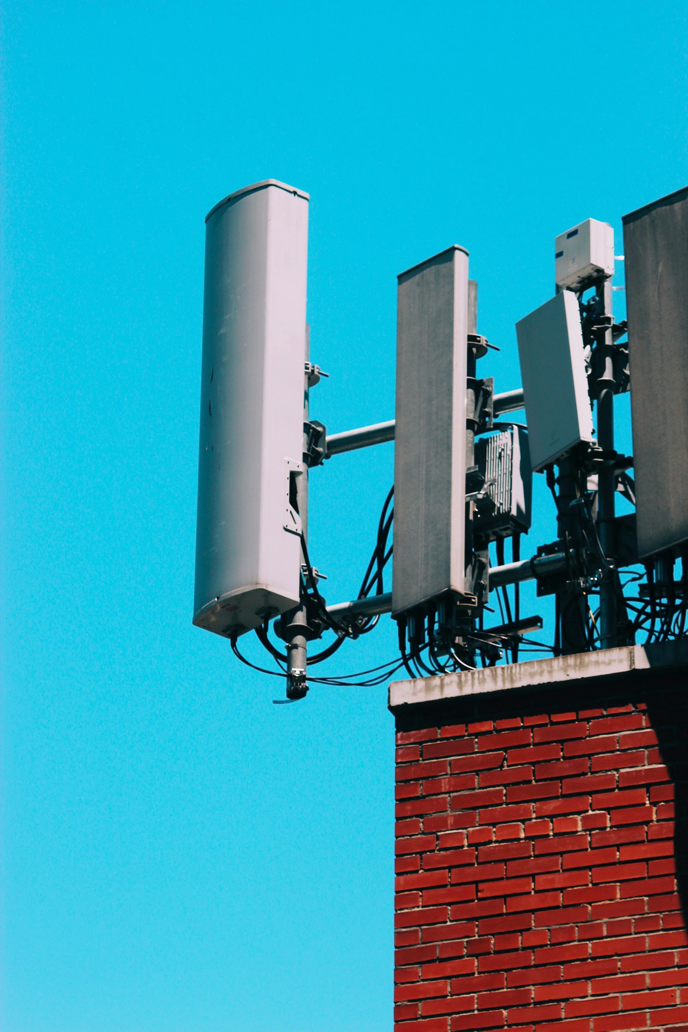 Cellular antennas and equipment mounted on a rooftop next to a brick chimney, with a clear blue sky in the background.