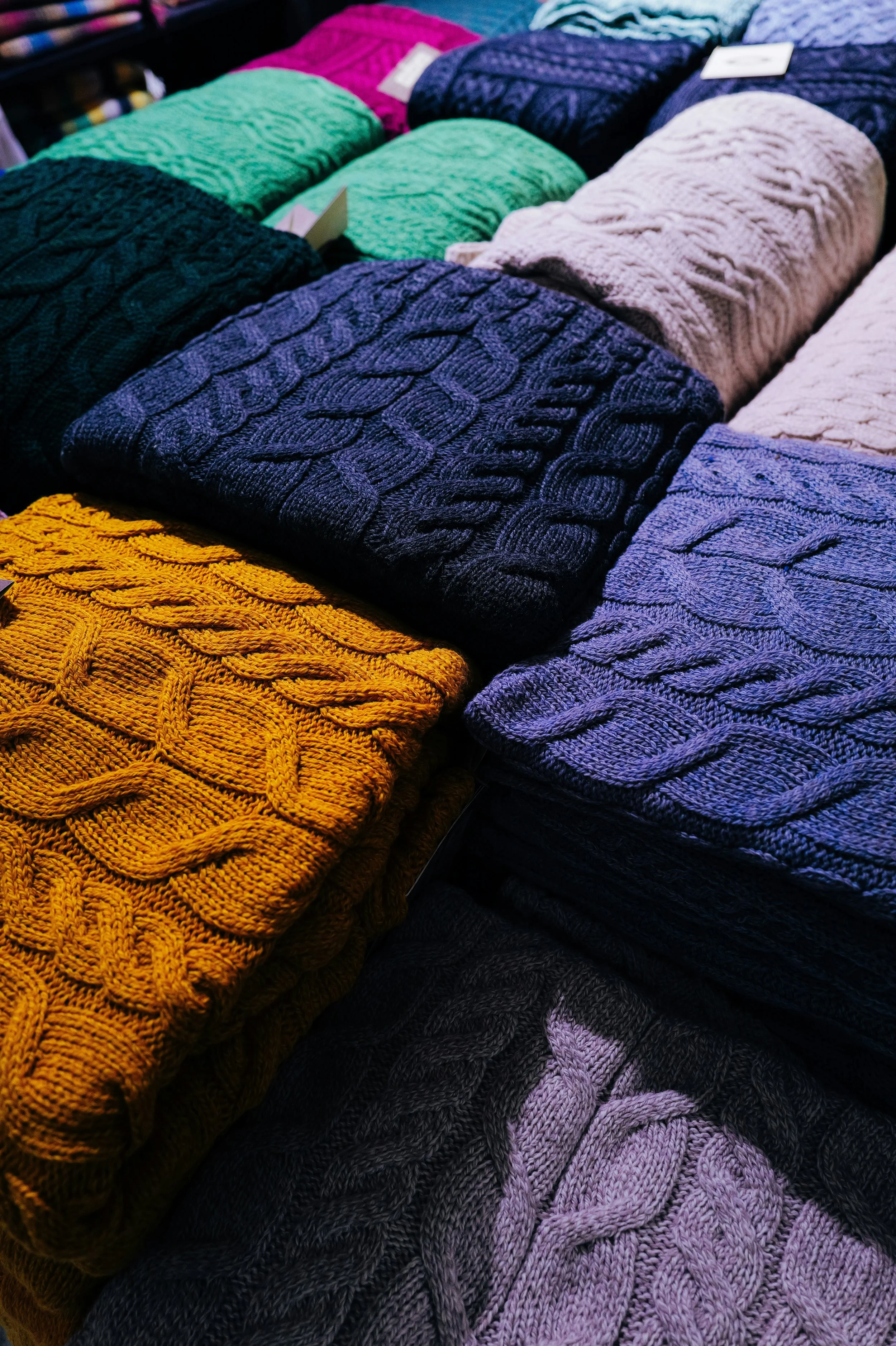 Various knitted sweaters in different colors including yellow, purple, white, dark blue, and green, stacked in a display.