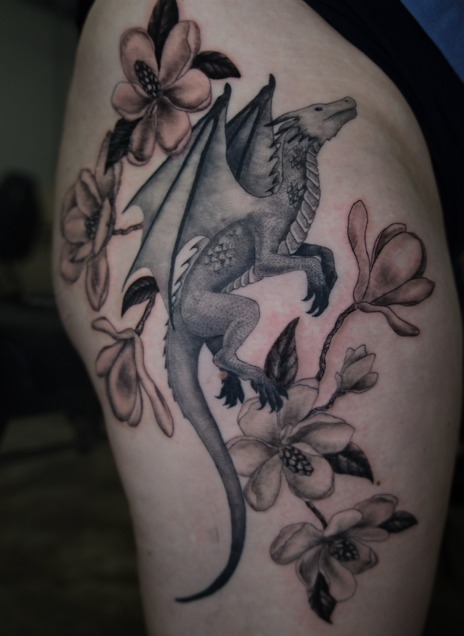 Tattoo of a dragon surrounded by pink flowers on person's upper thigh.