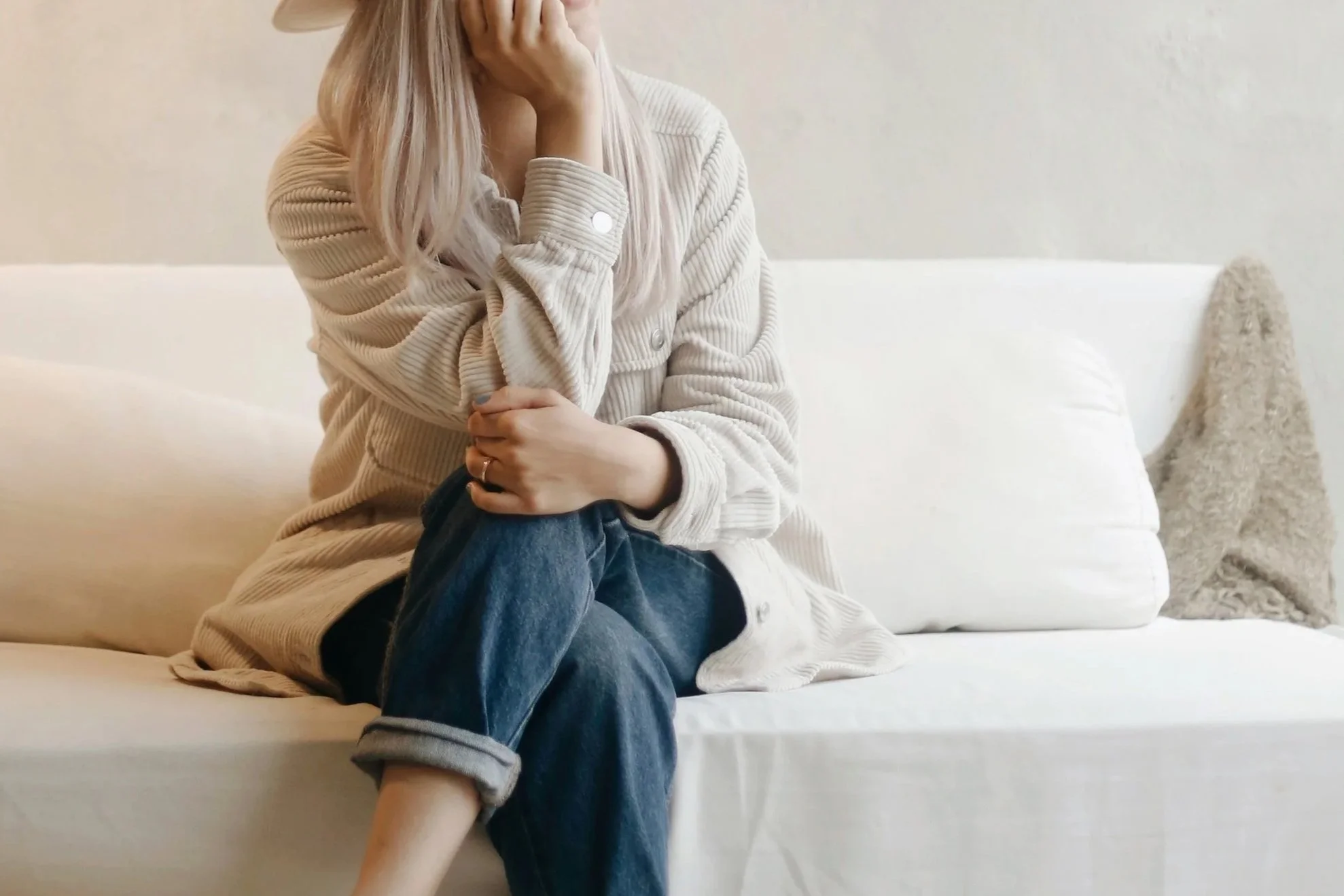 Woman sitting on couch, wearing jeans and a neutral colored jacket.