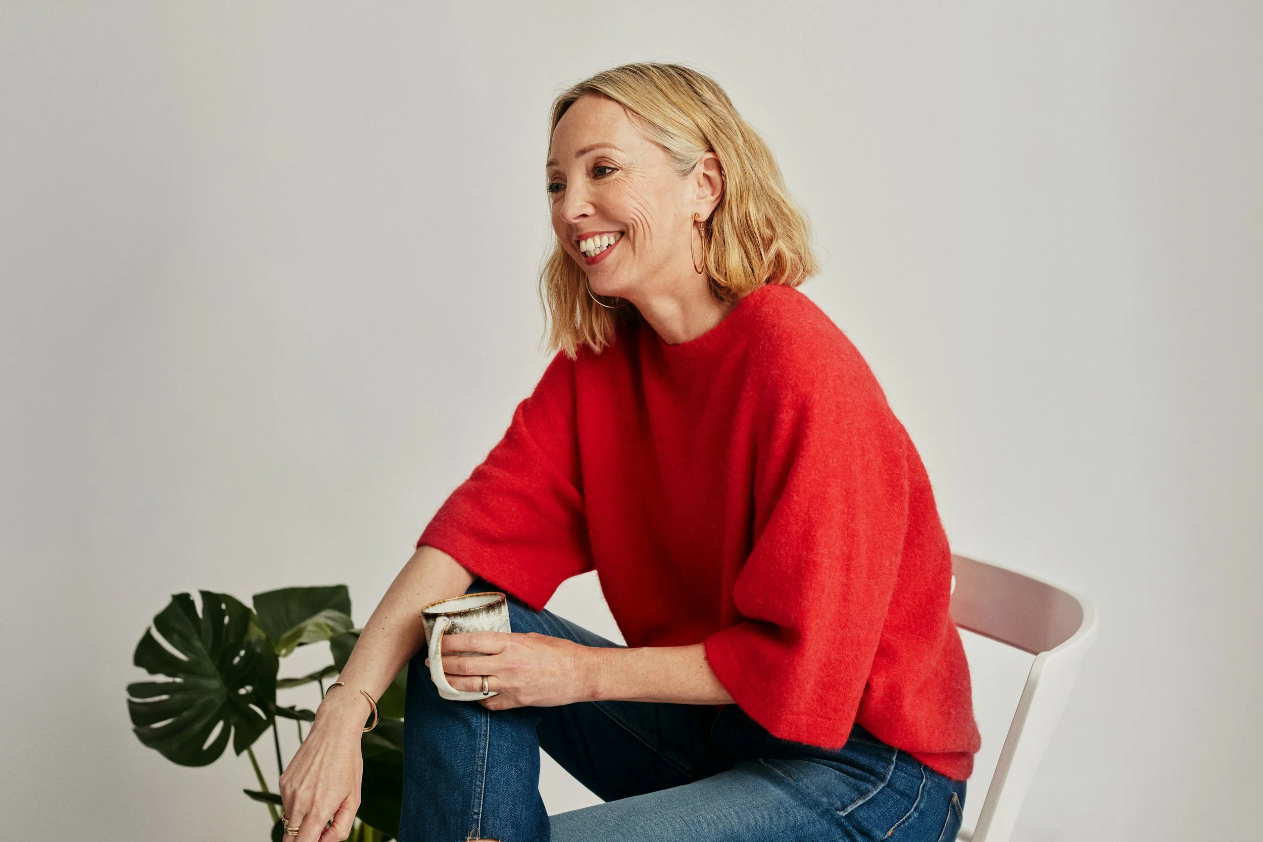 Middle aged woman with blonde hair enjoying coffee, wearing a red sweater in front of a white background. Arcadia Women's Wellness Modern Health Practice - Scottsdale Arizona