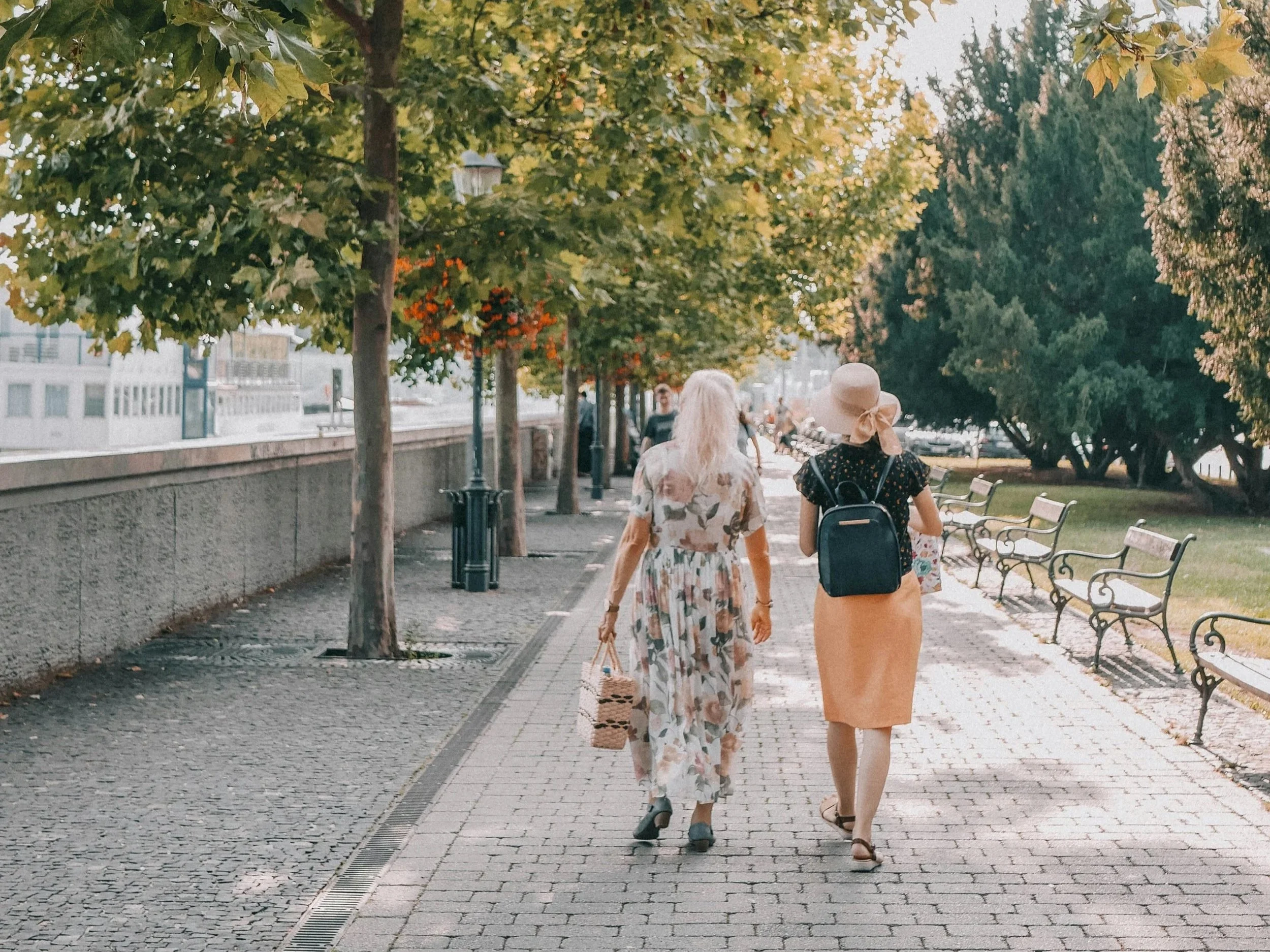 Two women walking together down a city garden sidewalk.