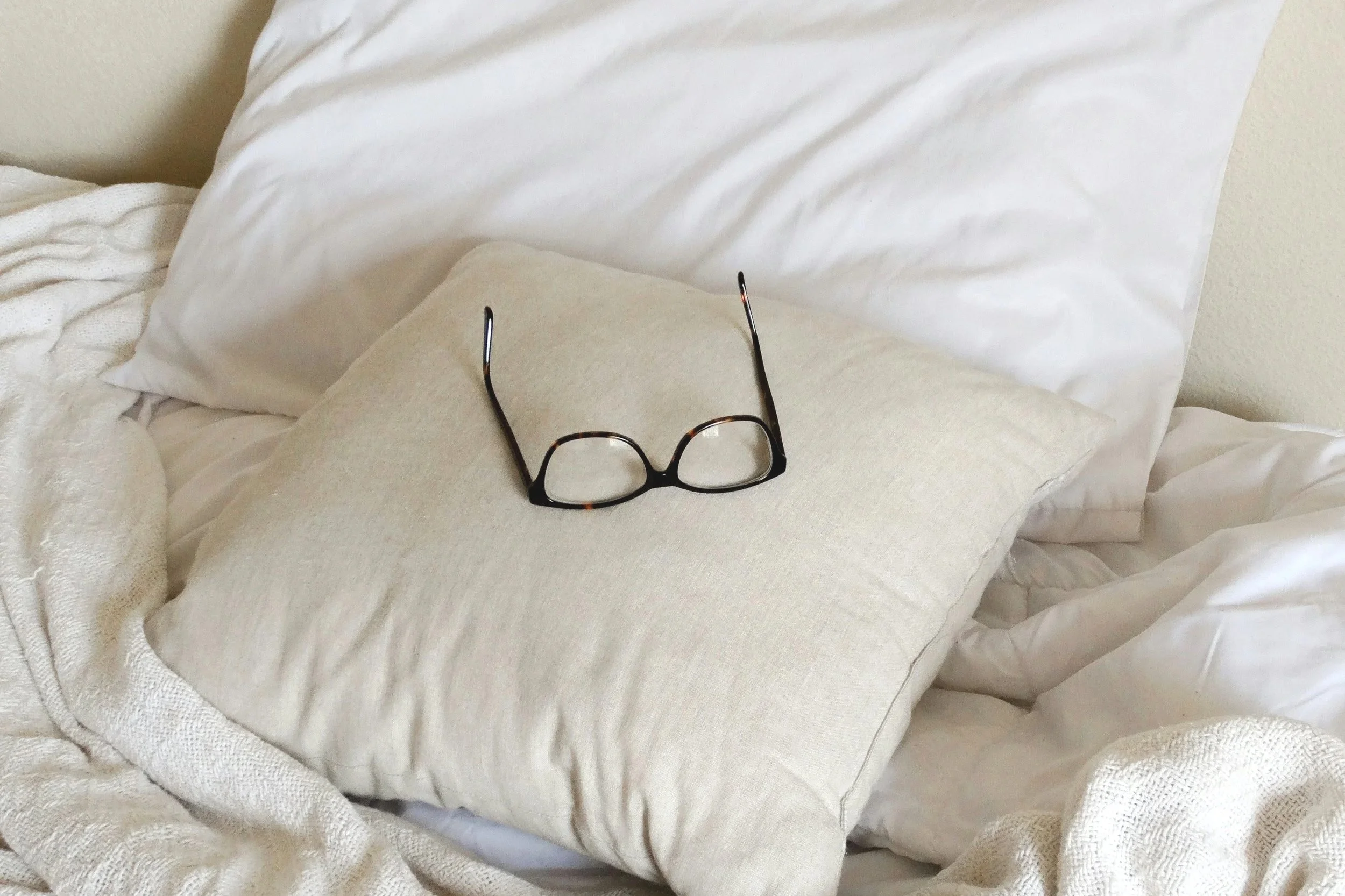 Glasses sitting on pillows on a bed.