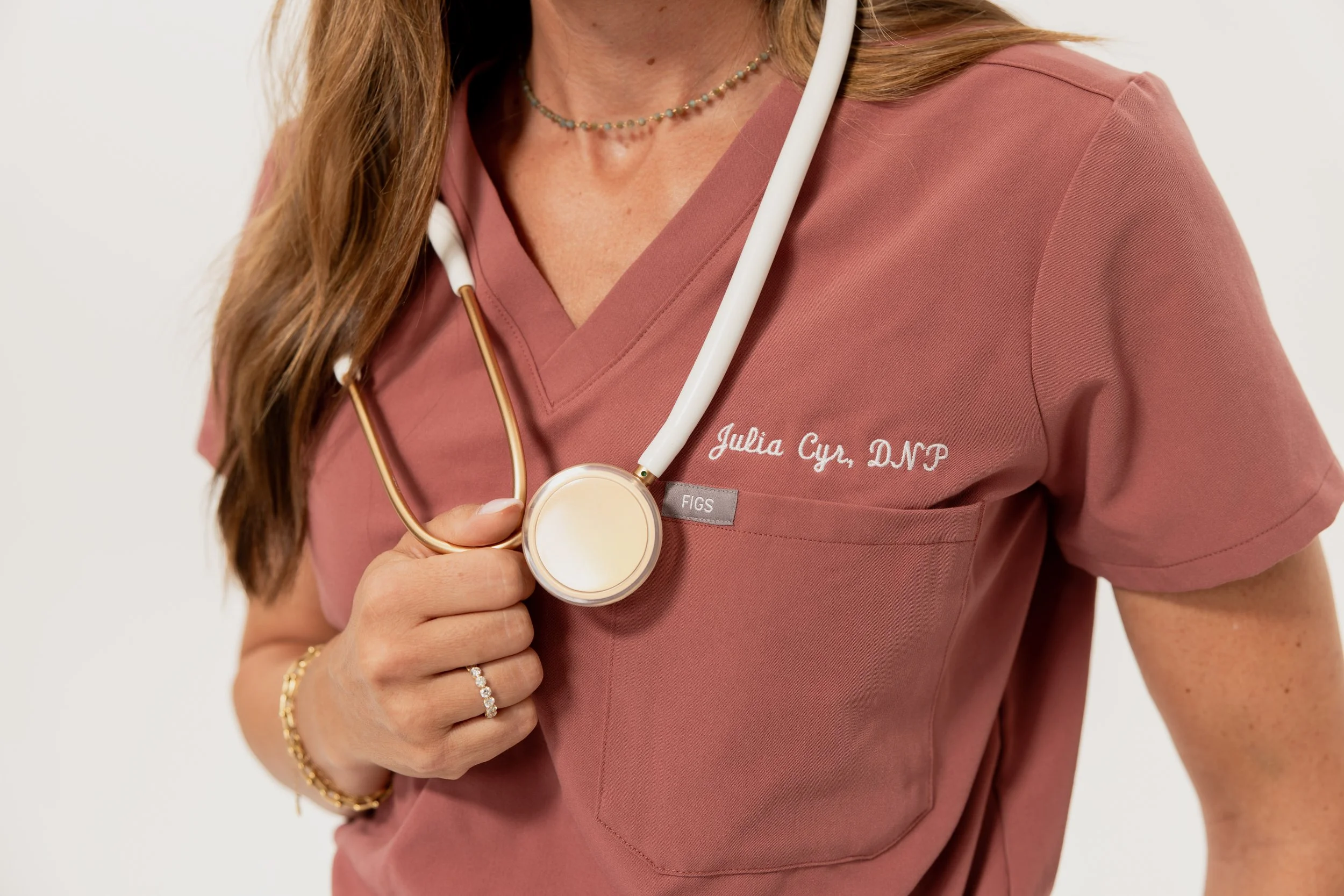 Close up image of a woman wearing pink scrubs and holding a stethoscope. Arcadia Women's Wellness PCOS and Endometriosis - Phoenix Arizona