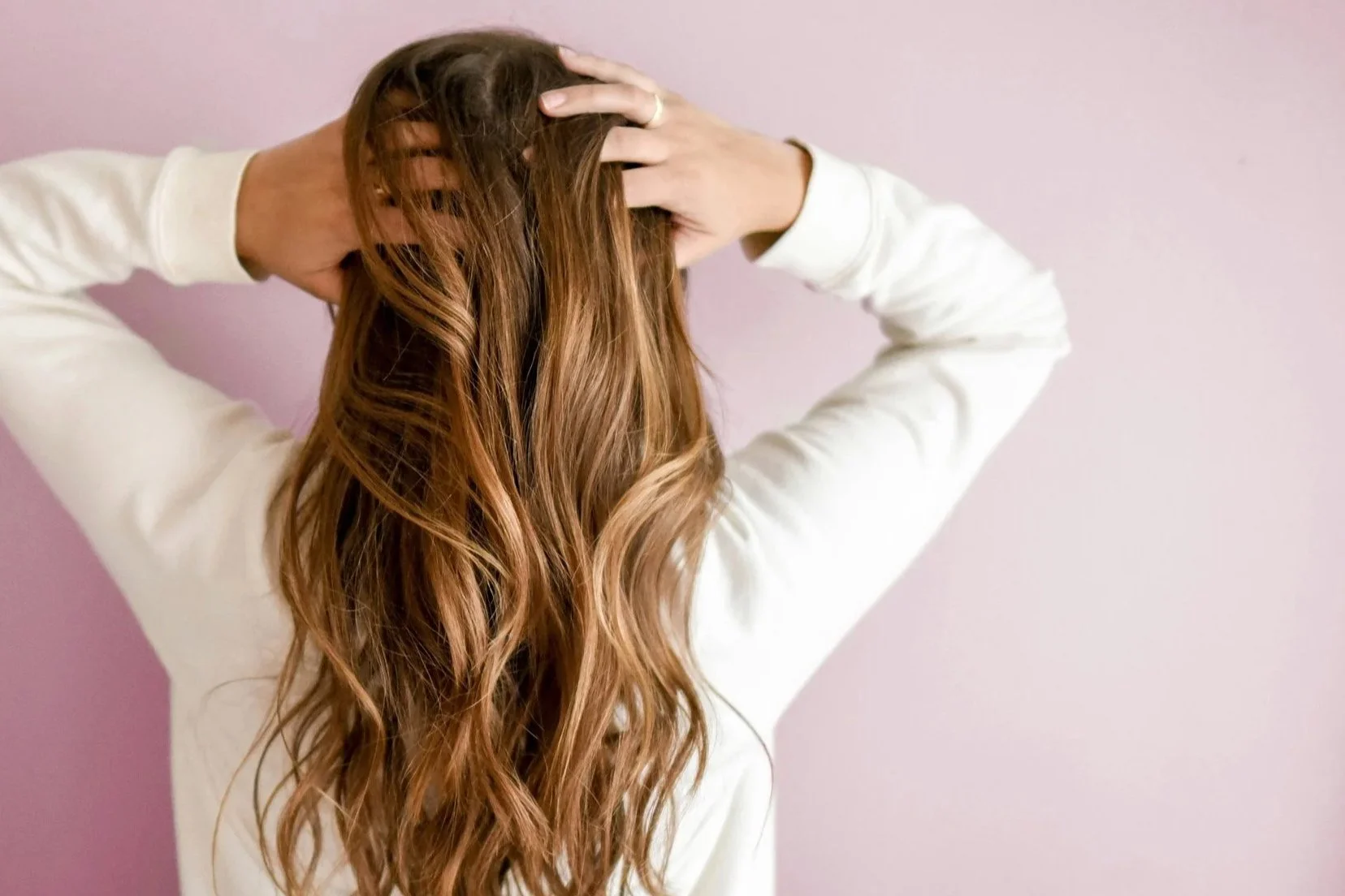 Woman anxiously holding her head in front of a mauve backdrop.