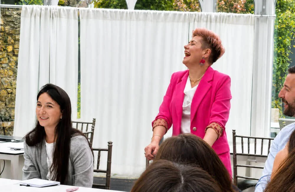 Ciara Crossan laughing as she facilitates a workshop with seated participants in a bright meeting room.