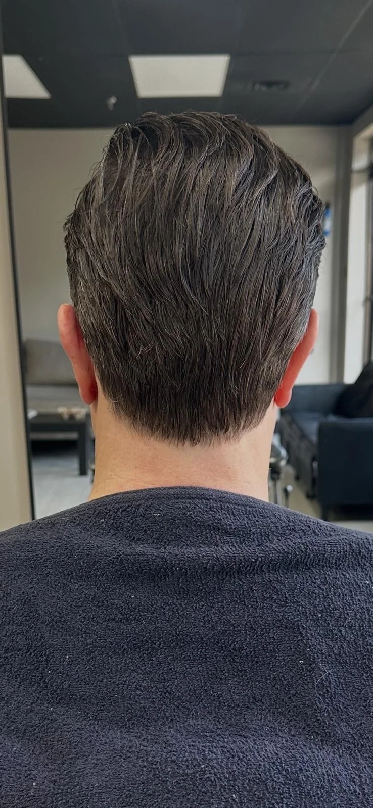Back of a man's head with neatly styled short brown hair in a salon or barber shop.