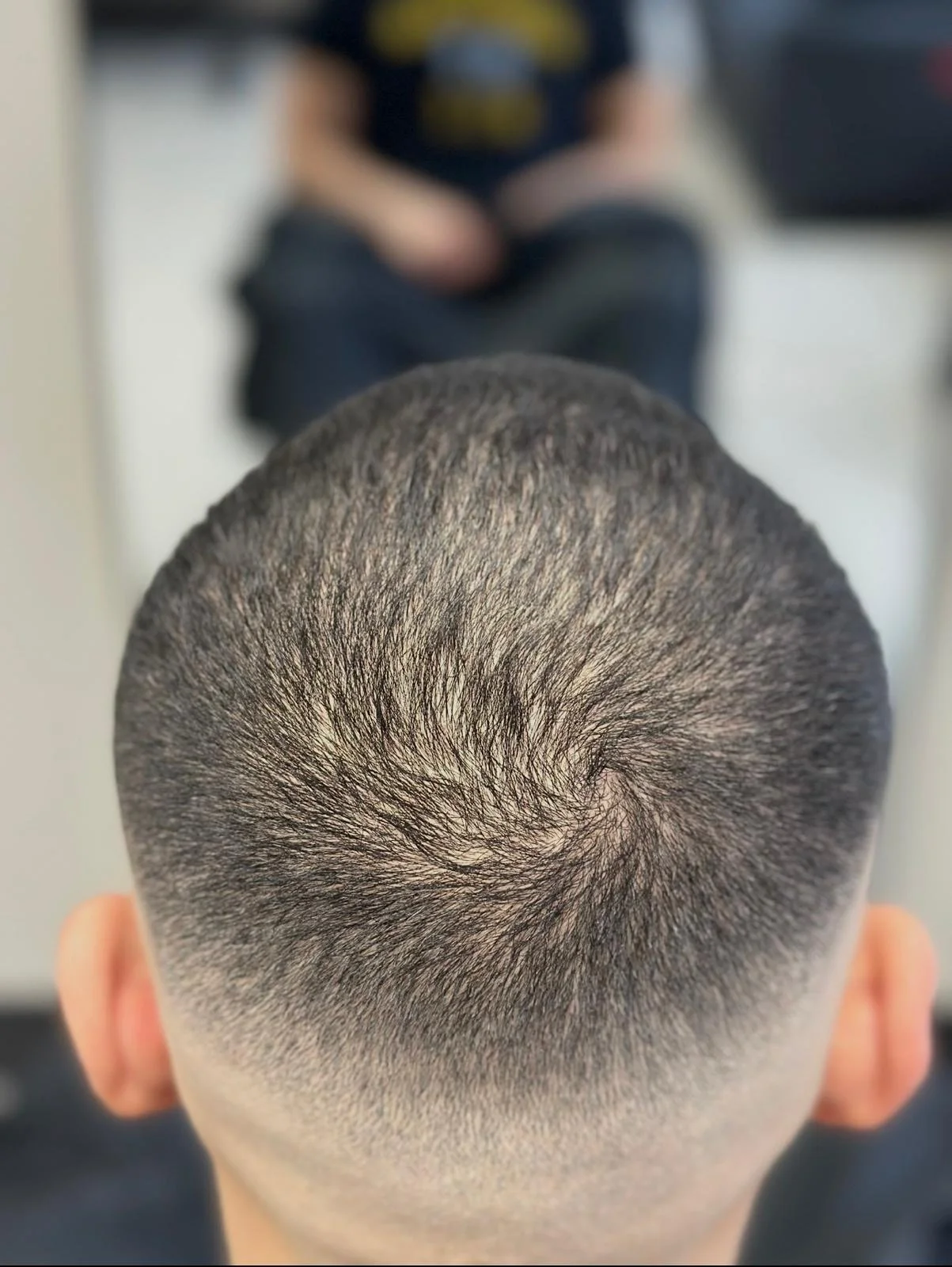 Top view of a person's head with a spiral pattern buzz cut hairstyle showing short, evenly cut hair.