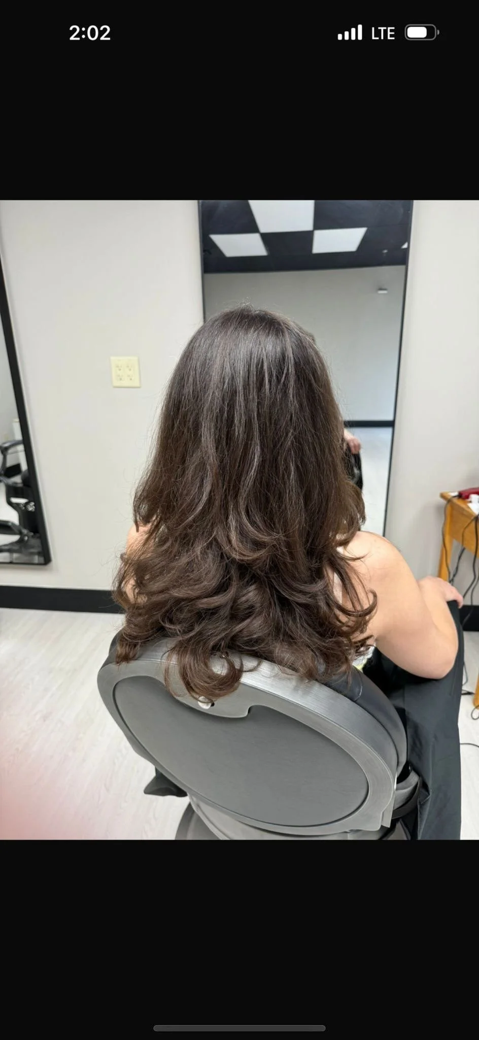 Woman with shoulder-length brown wavy hair sitting in a salon chair