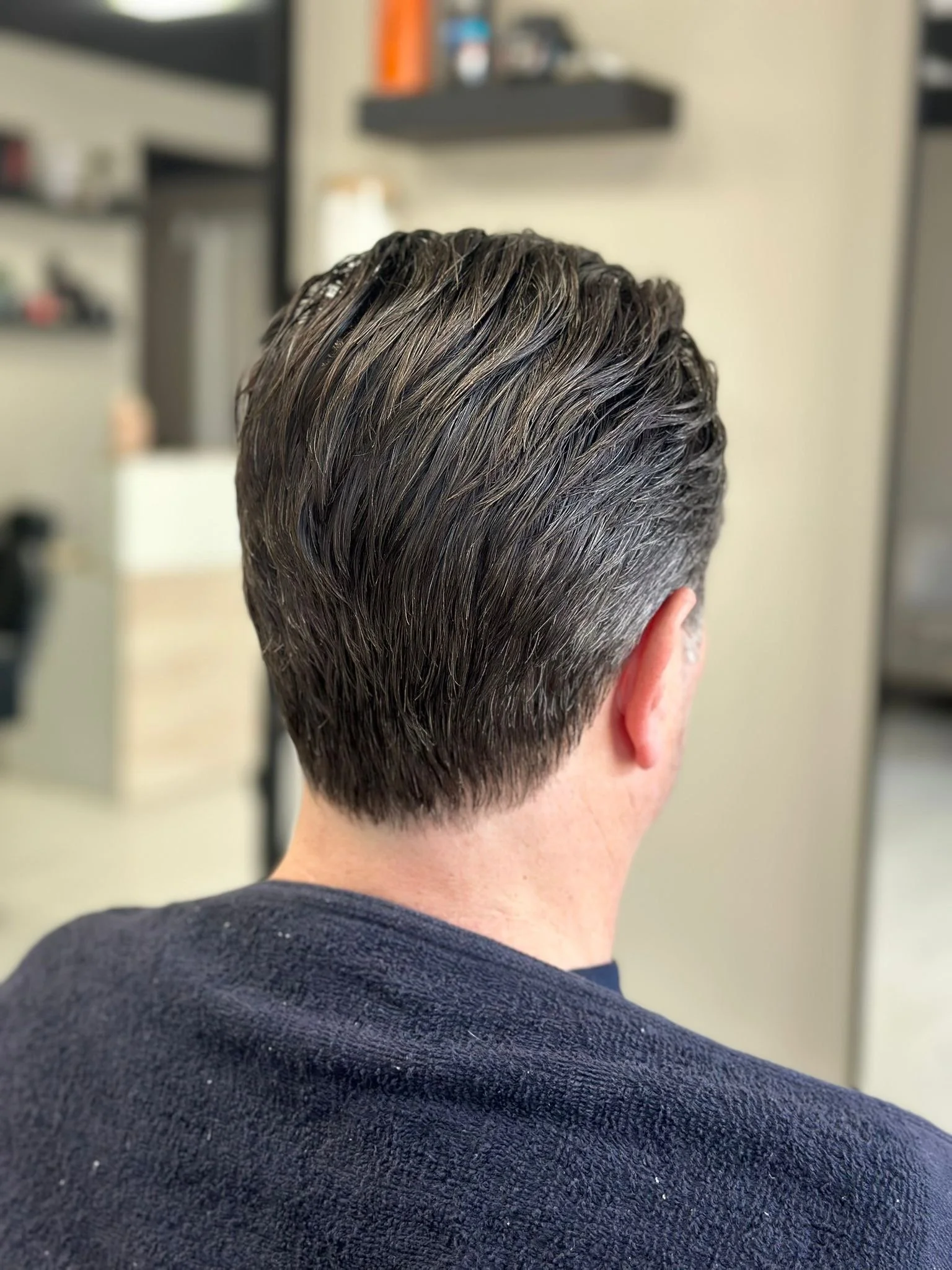 Back of a person's head with dark, wavy hair and a short, tapered haircut, wearing a dark blue sweater.