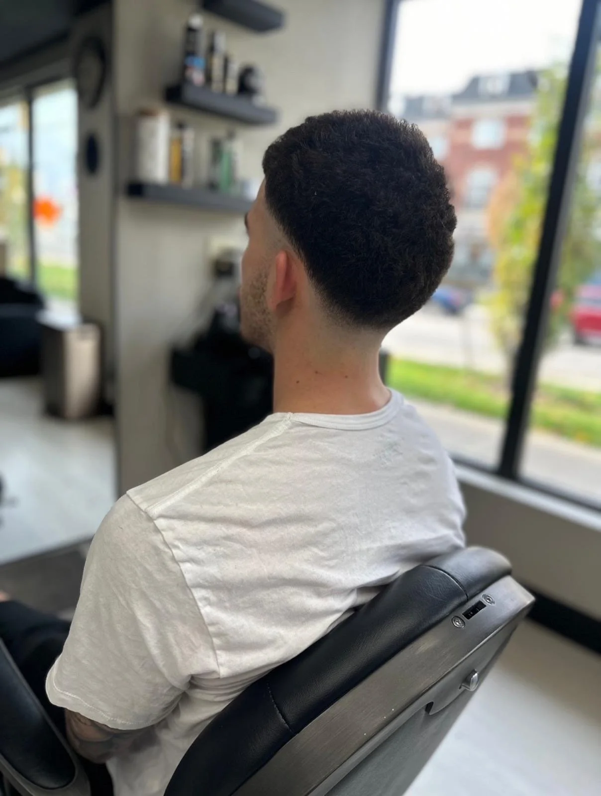 Man with a fresh haircut sitting in a barber shop chair near a window.