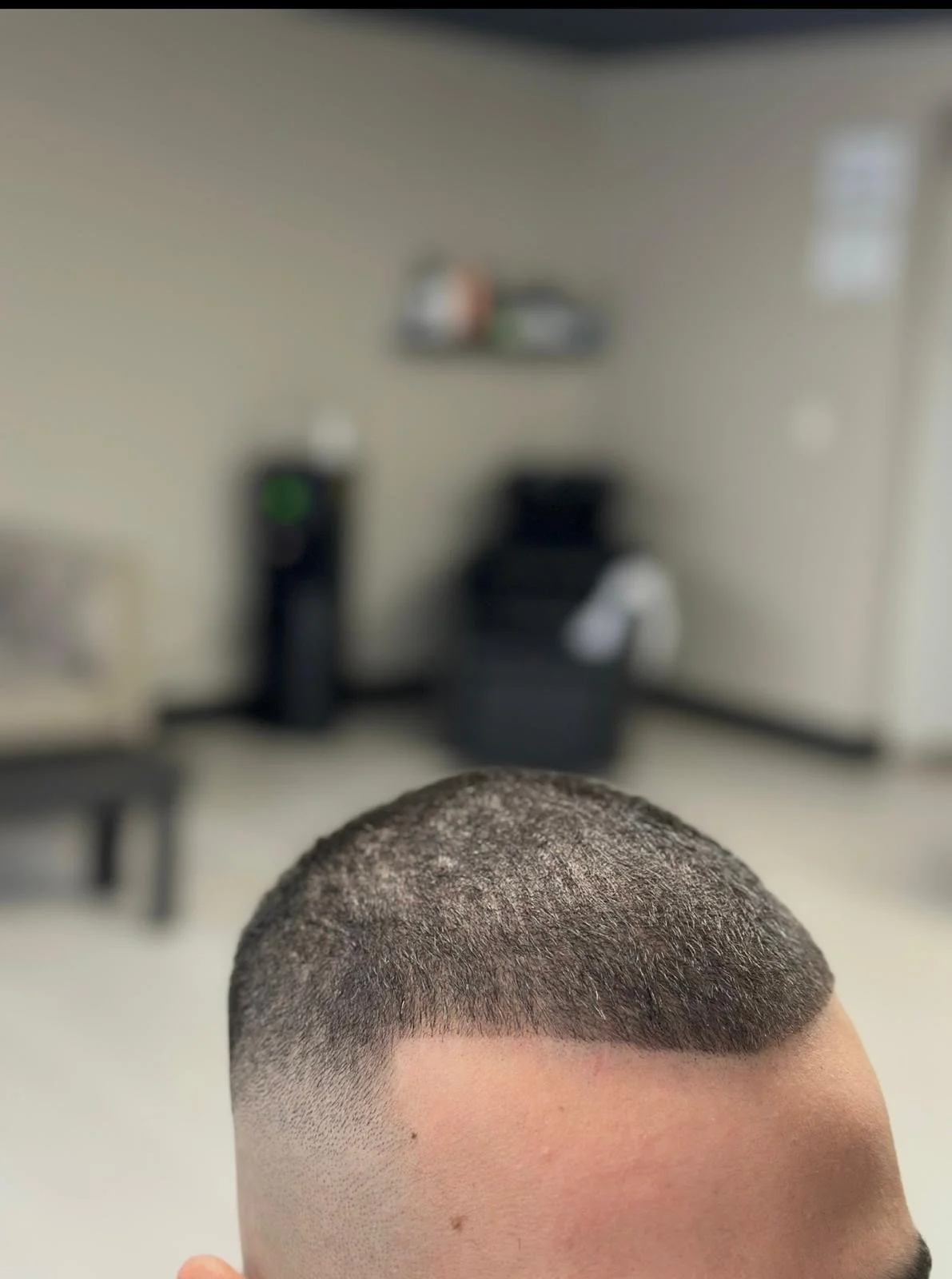 Close-up of a freshly shaved head with a buzz cut, against a blurred background of a barbershop or salon interior.
