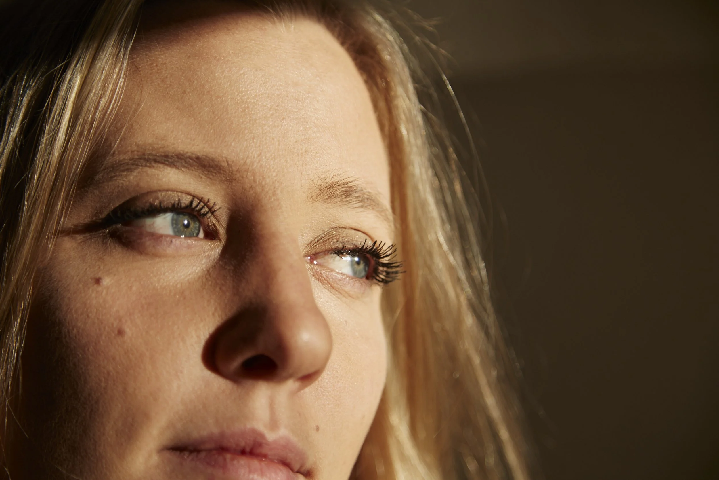 Close-up of a woman's face with blue eyes and blonde hair, illuminated by natural light.