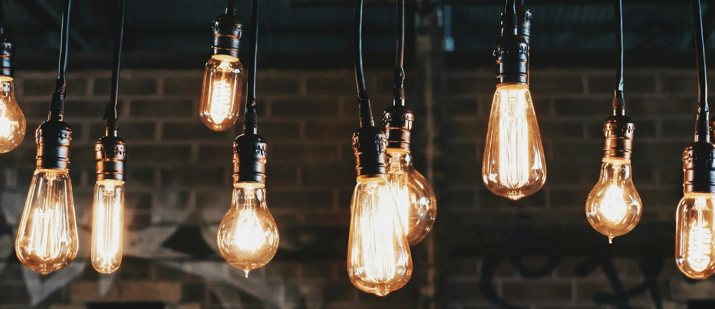Multiple Edison-style filament light bulbs hanging from cords against a brick wall background.