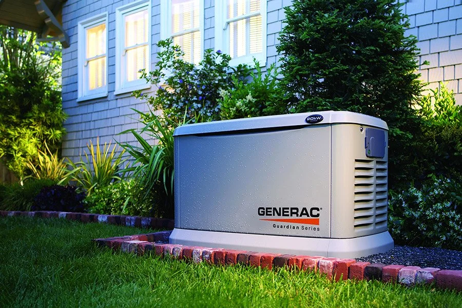 A Generac Guardian Series backup generator outside a house surrounded by plants and grass.