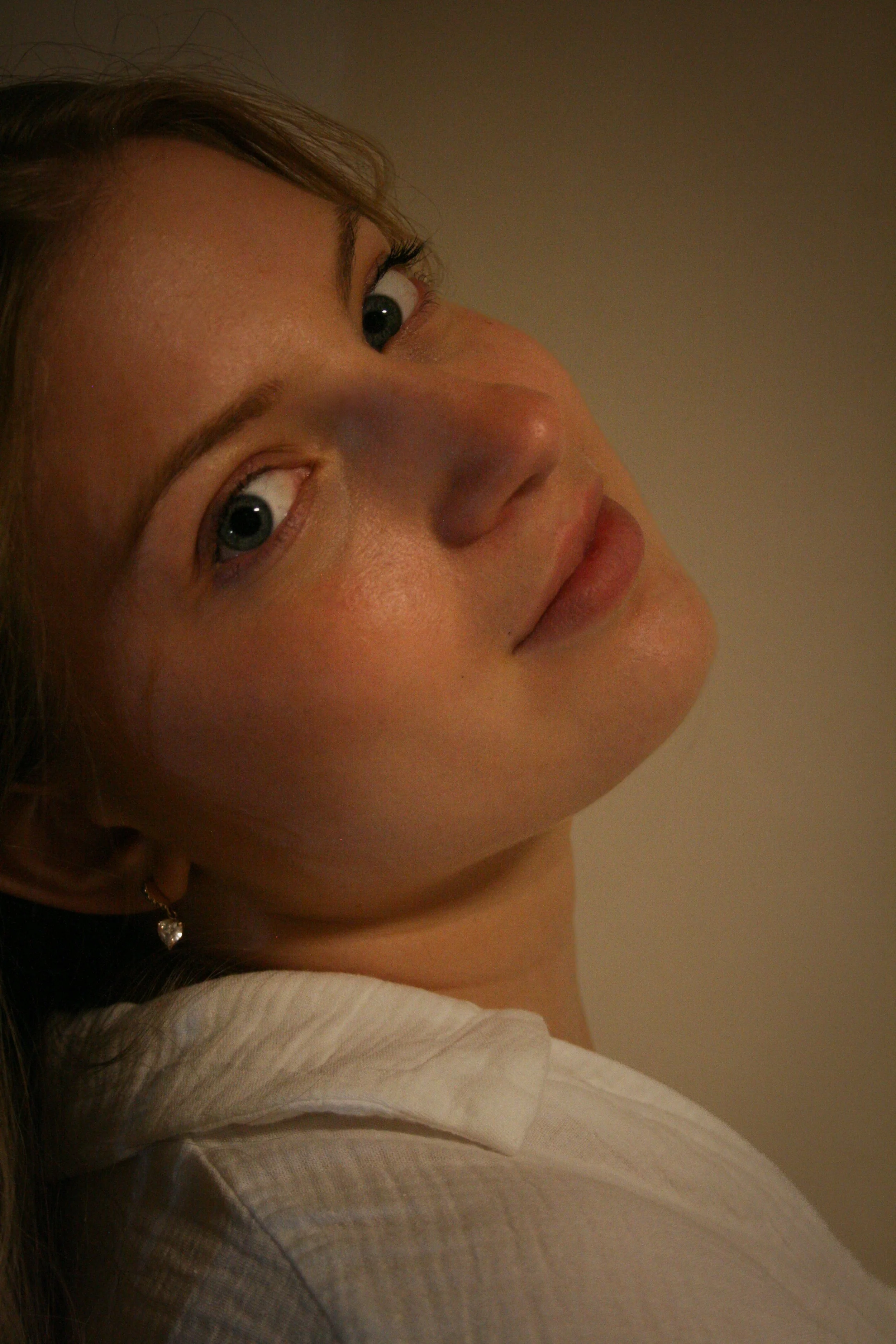 Photo d'une femme avec des yeux bleus, souriant légèrement, portant une boucle d'oreille en forme de cœur.