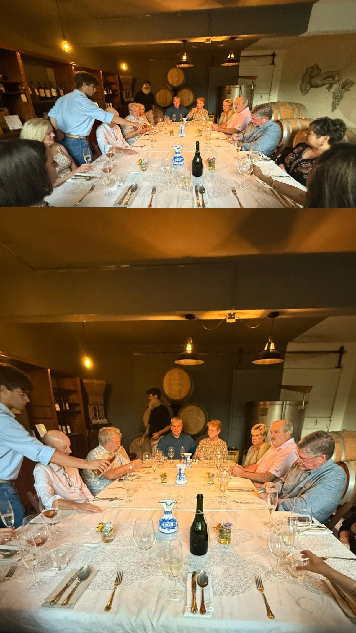 Group of people seated around a dining table in a restaurant or winery, with wine bottles and glasses, and wooden barrels in the background.
