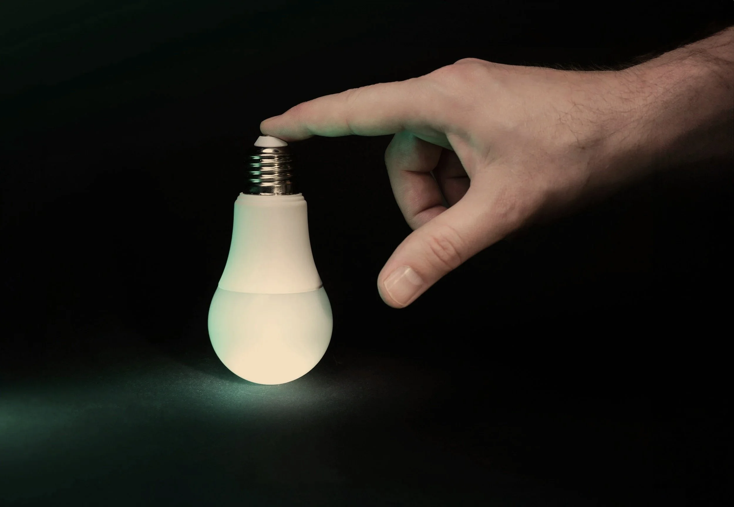 A hand holding a small light bulb emitting a soft glow, against a dark background.
