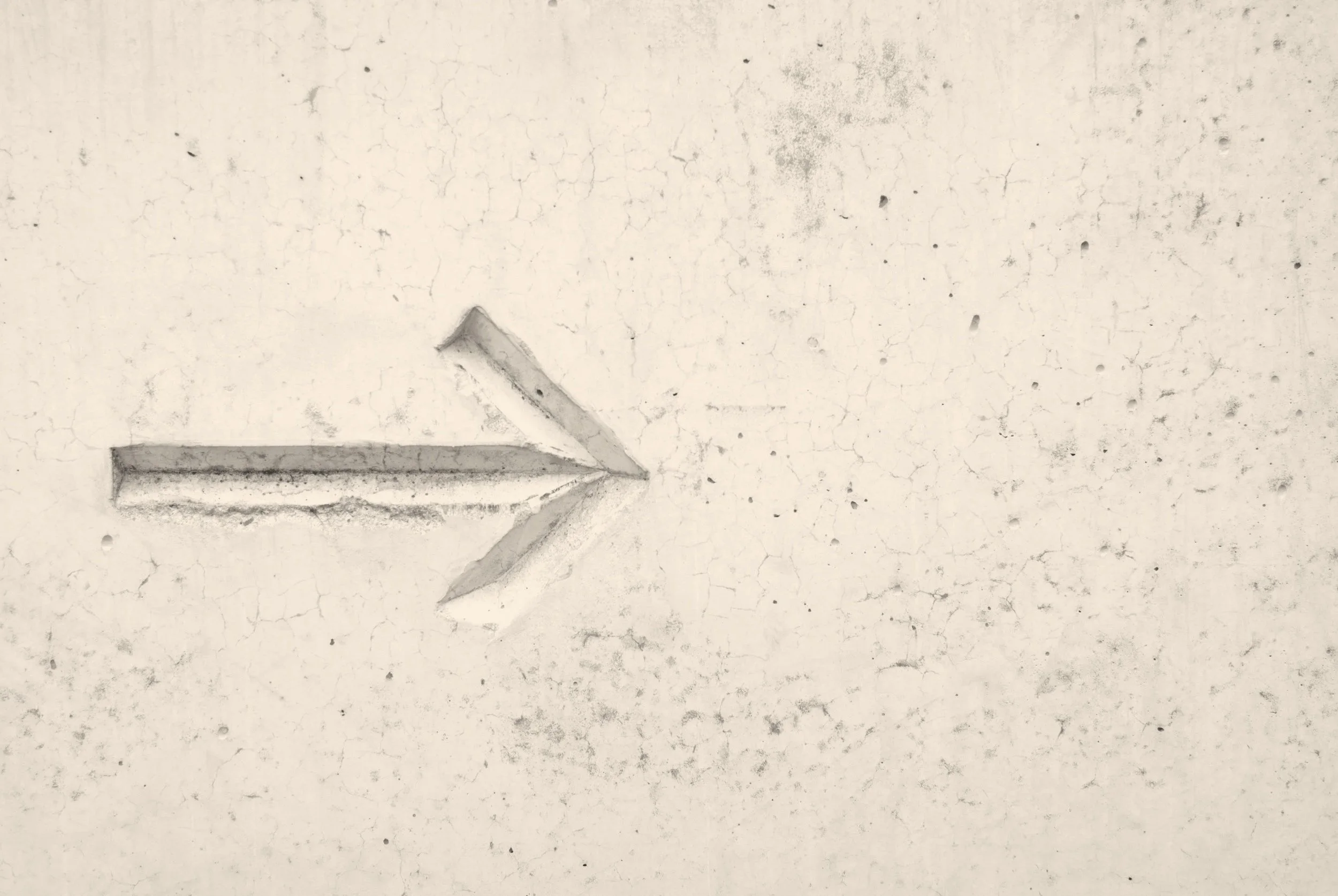 A close-up of a white, cracked wall with a metal arrow-shaped object embedded in it, pointing to the left.