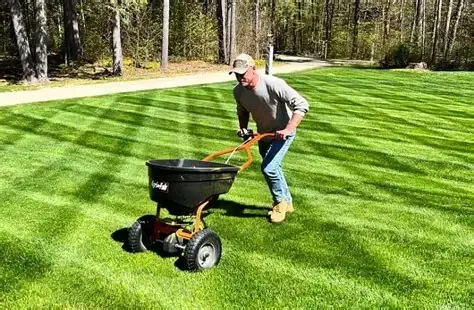 A man in a gray hoodie and jeans pushing a lawn watering hose on a black garden cart with large wheels on a well-maintained green lawn.