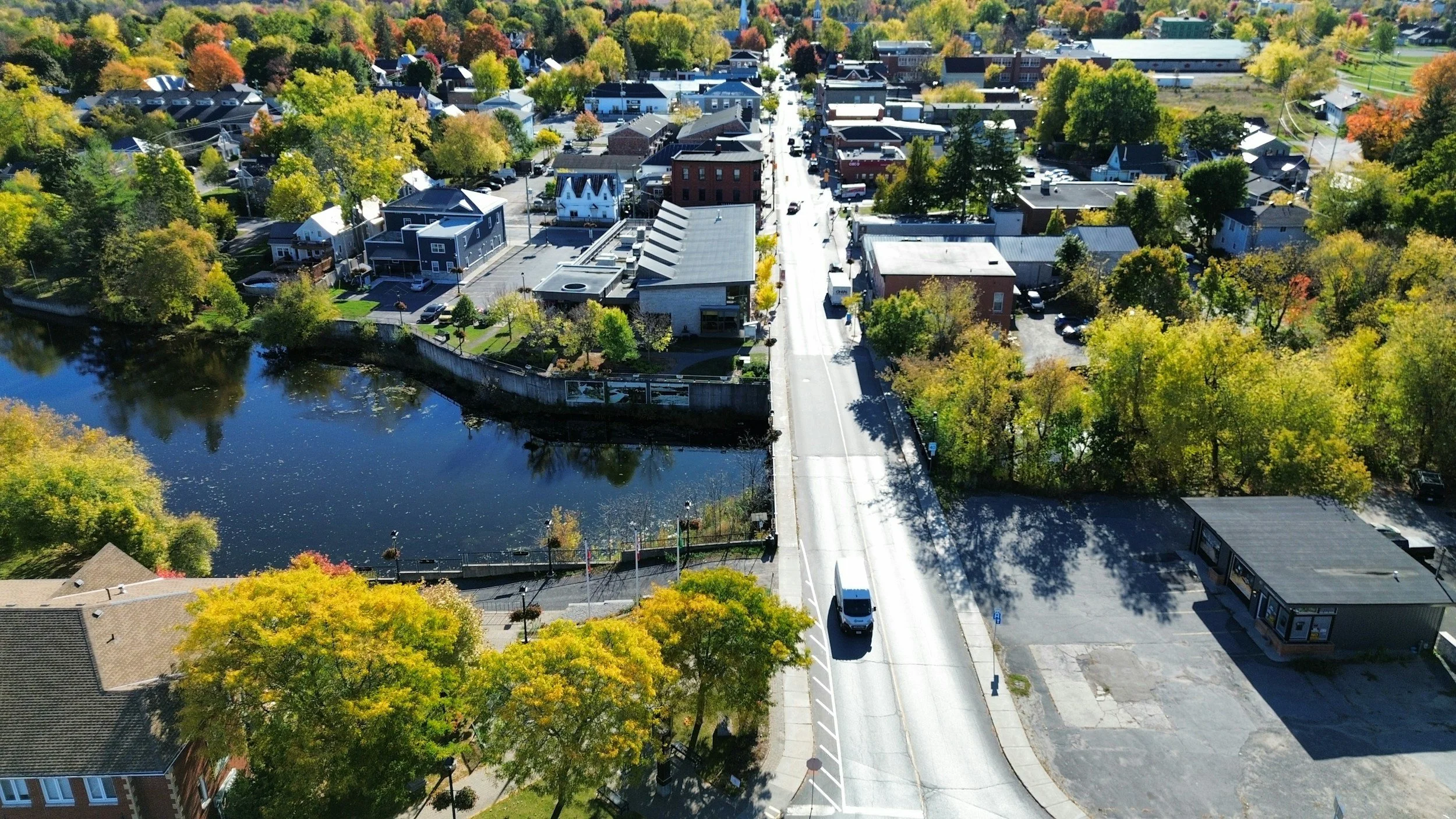 Aerial view of a small town with colorful autumn trees, a river, and a main street with parked cars and buildings.