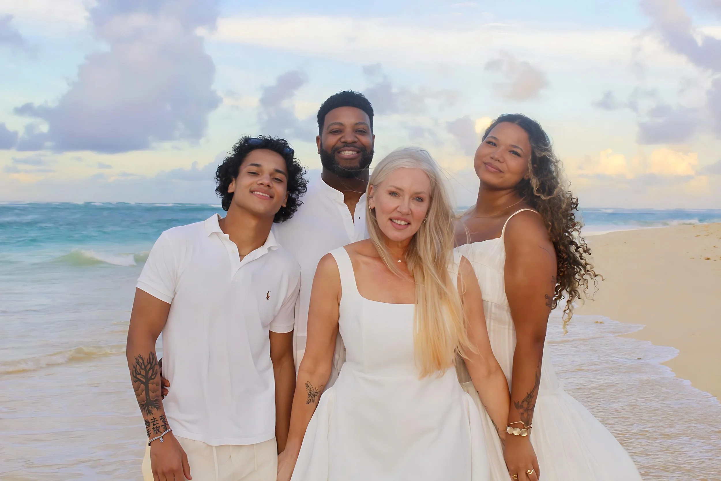 Amy, her husband, and two kids standing on a beach with the ocean and cloudy sky in the background.
