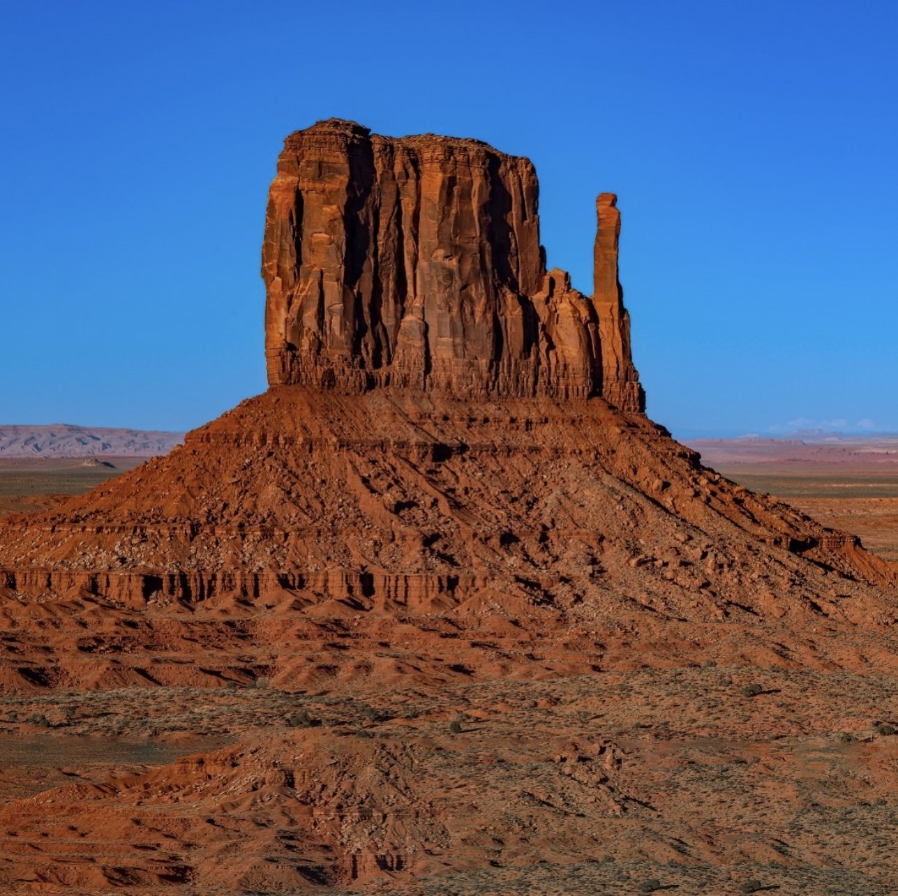 A large red rock formation in a desert landscape with a clear blue sky.