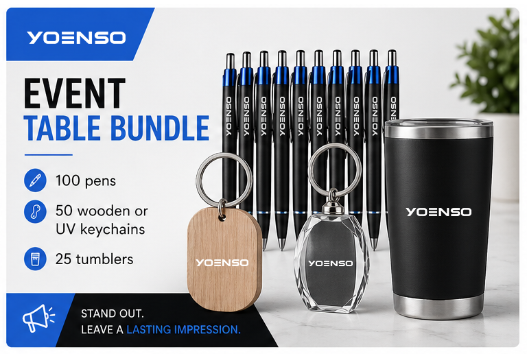 A promotional display for the YOENSO event table bundle, including 100 pens, 50 wooden or UV keychains, 25 tumblers, a black tumbler, and a few decorative plant leaves in the background.