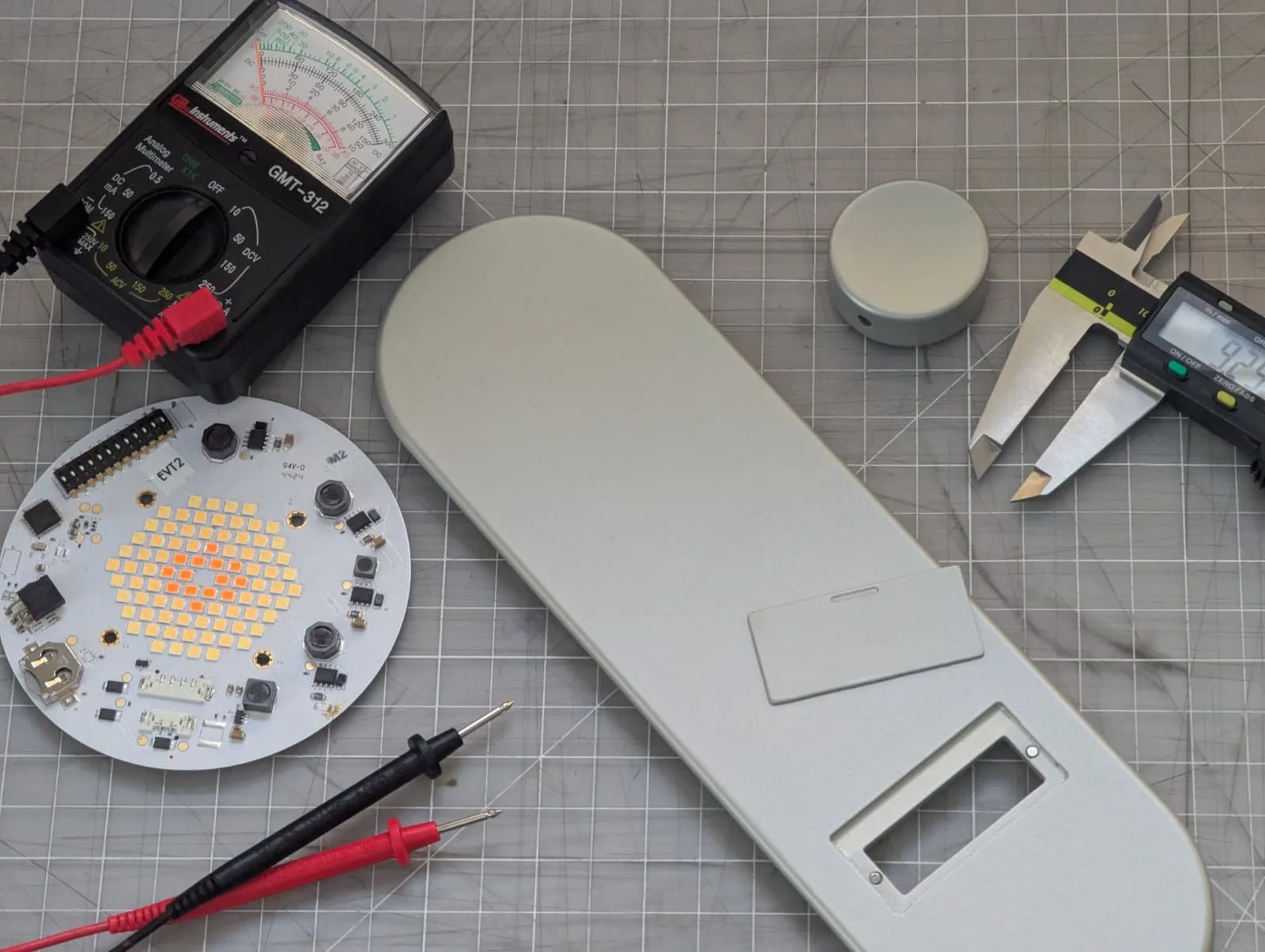 Electronics workbench with circuit board, multimeters, screwdriver, and partially assembled device.