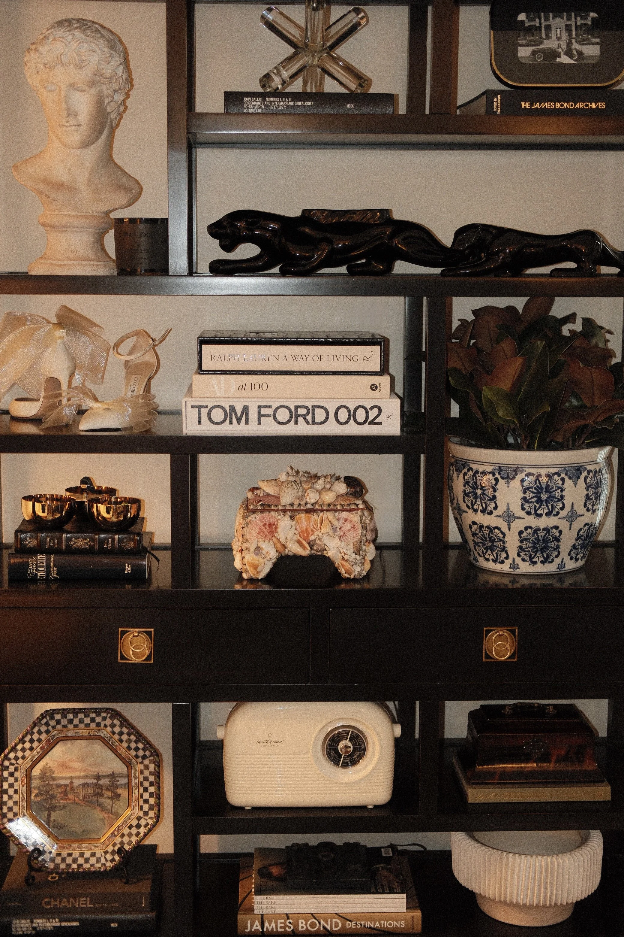Henredon display shelf, classic bust sculpture, seashell box, blue and white chinoiserie planter, Ralph Lauren, Tom Ford, and Architectural Digest books, tortoise shell box, Jimmy Choo shoes, MacKenzie-Childs plate, decorative accents.