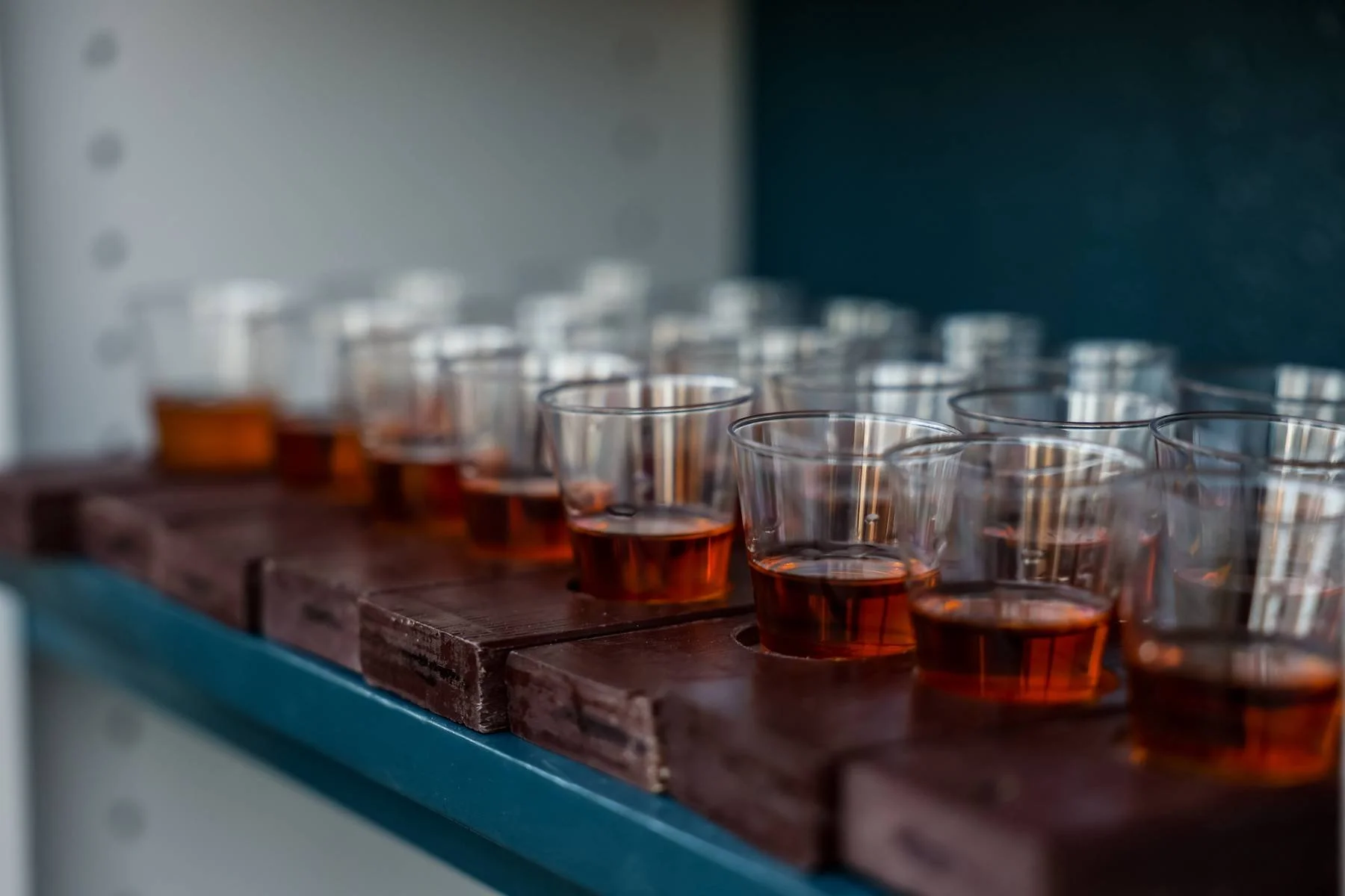 Multiple small plastic cups filled with a reddish-brown liquid arranged on a wooden shelf.