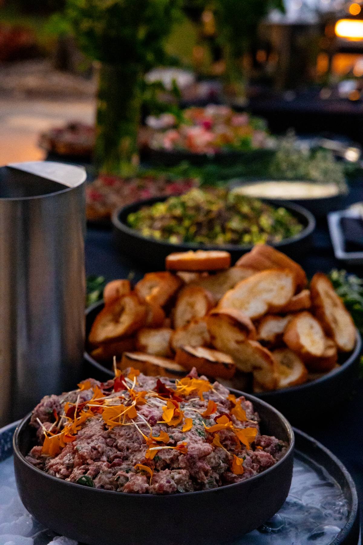 Outdoor buffet with bowls of salad, sliced bread, and various dishes on a table.