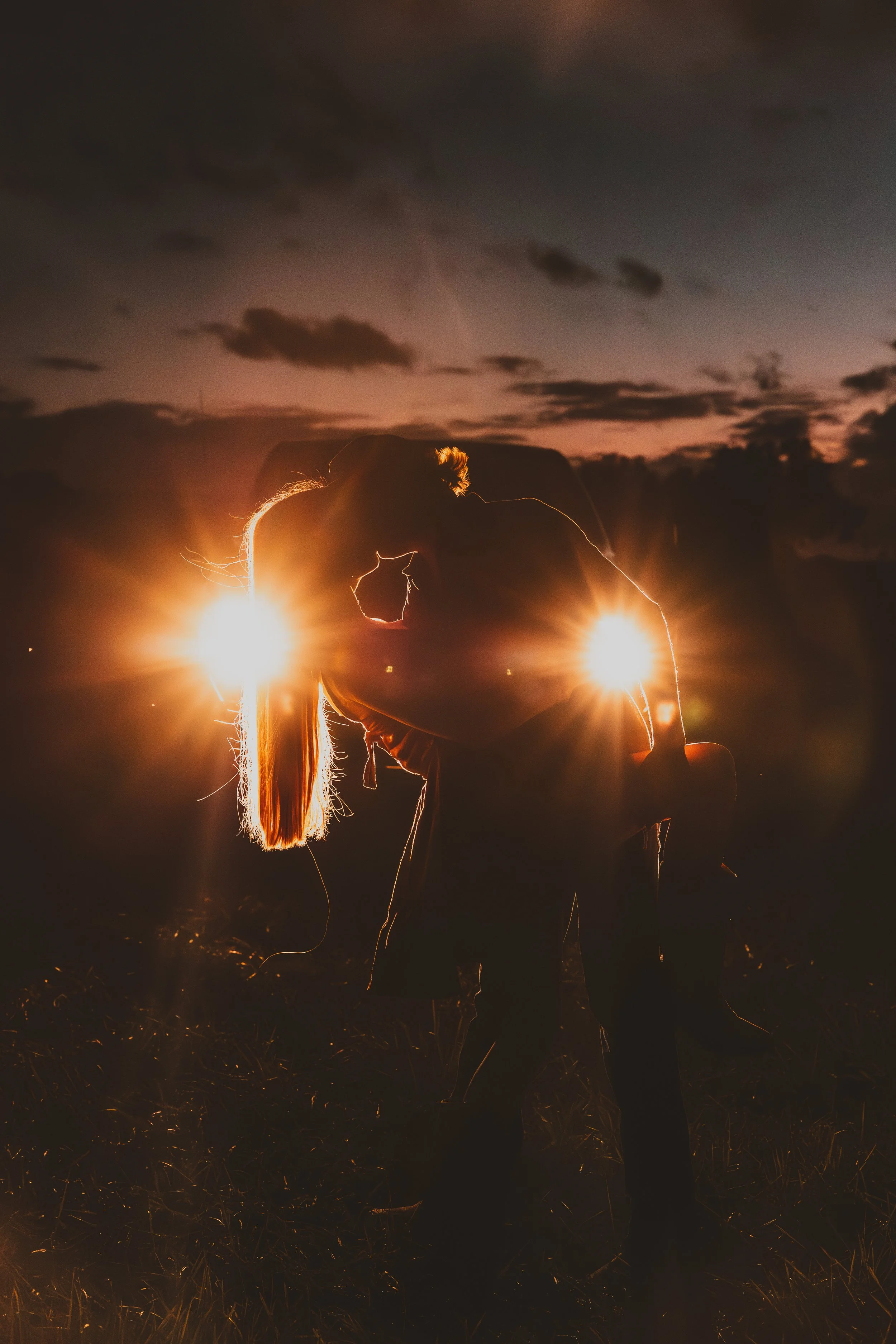 Silhouette of a couple kissing during sunset or twilight with the sky and clouds in the background, warm sunlight glowing around them.