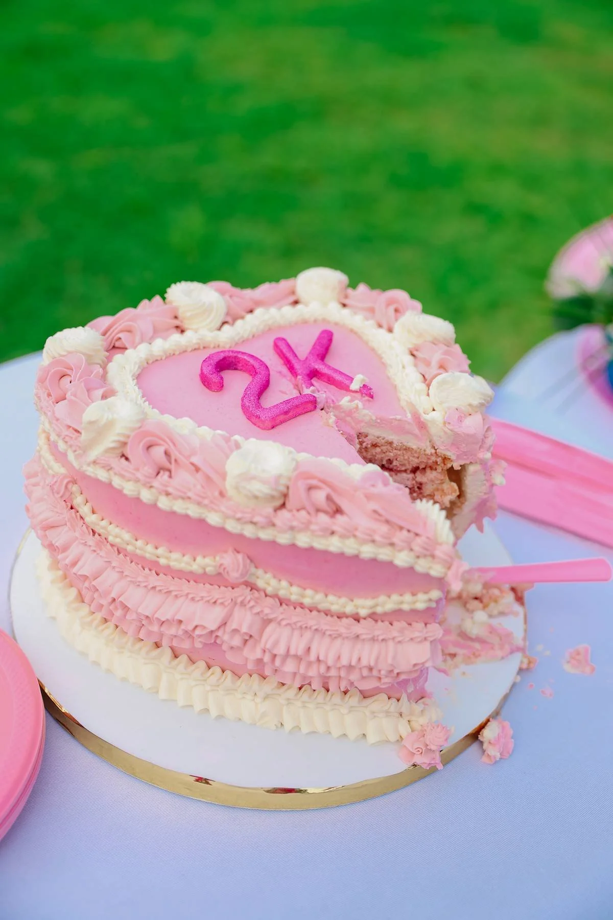 A heart-shaped pink birthday cake with white and pink frosting decorations, topped with pink number candles reading '2K', partially cut to show the inside layers.