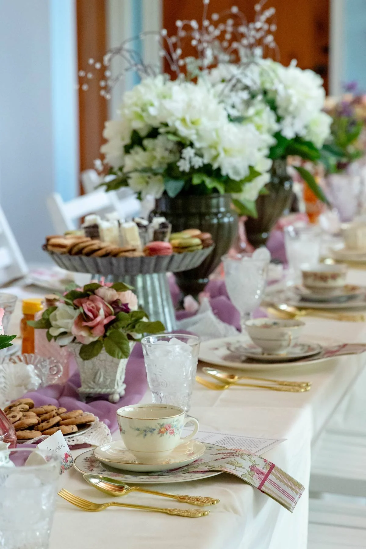 A beautifully arranged table set for a formal event with floral centerpieces, tea cups, dessert plates, and assorted cookies and macarons.