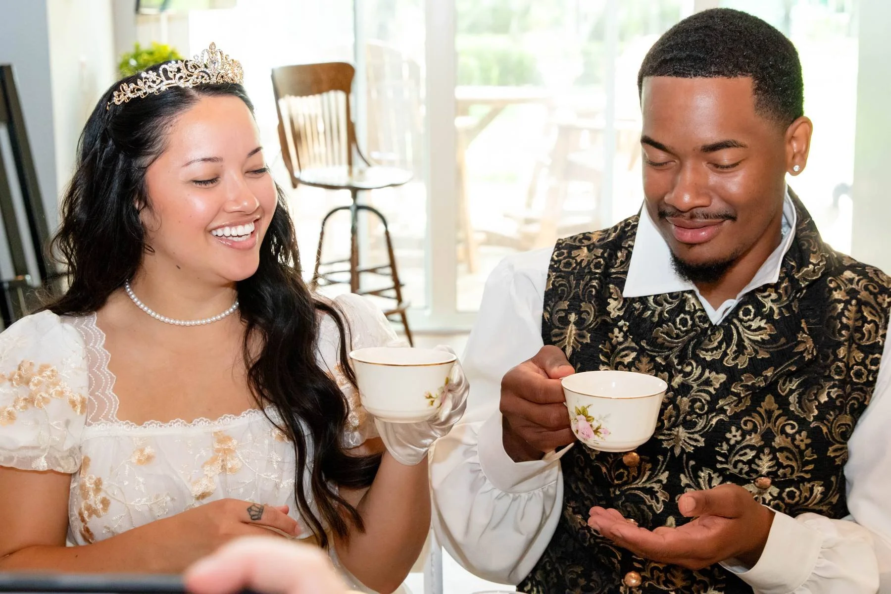 A bride and groom smiling and holding teacups during a celebration.