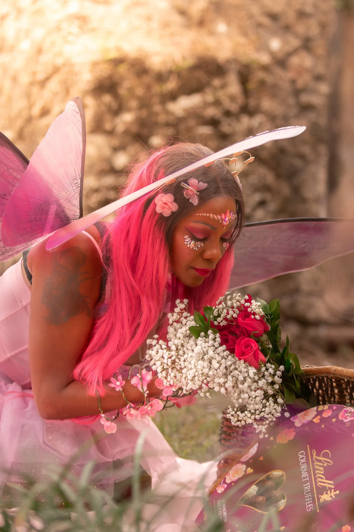 A woman with long pink hair and fairy wings holding a bouquet of pink and white flowers.