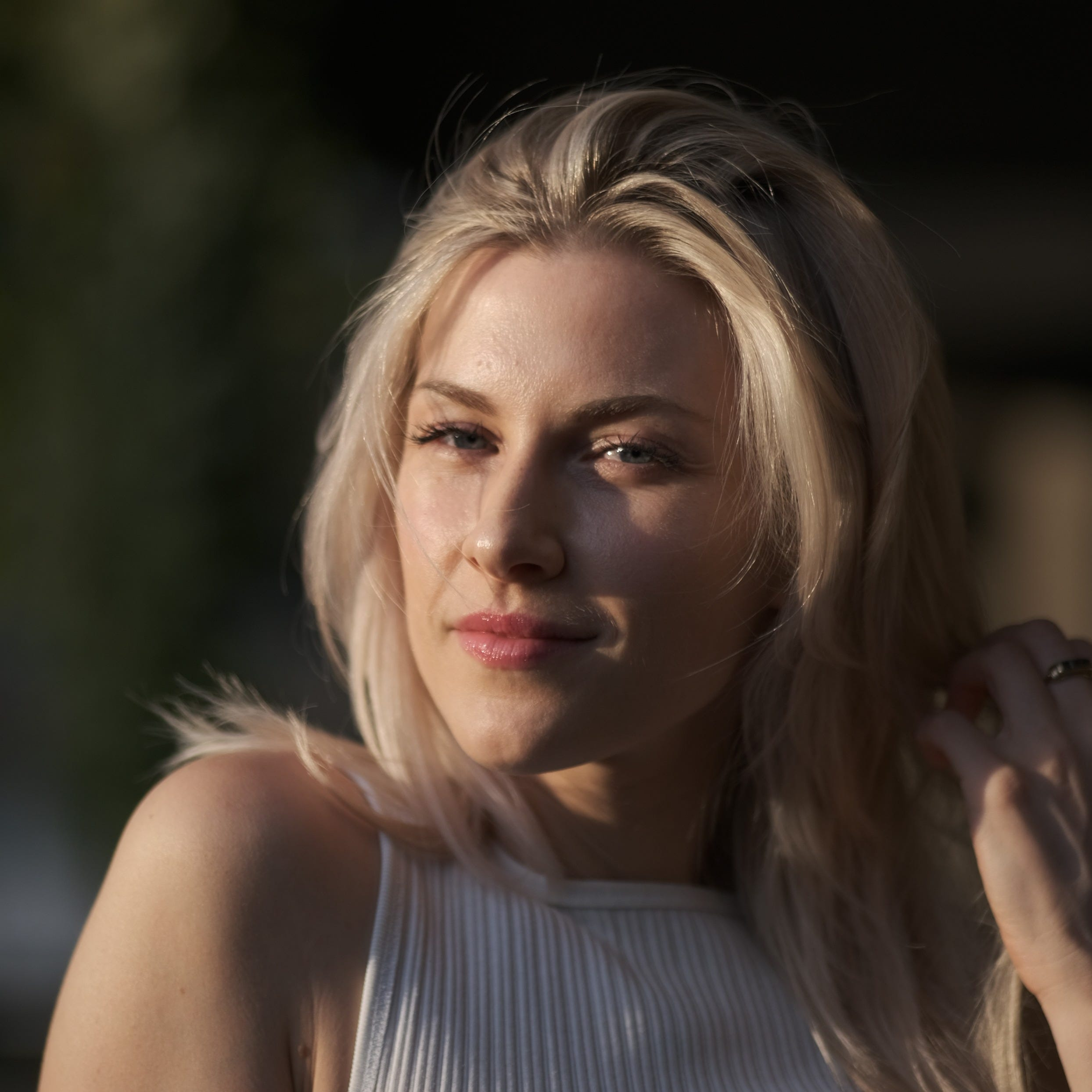 A blonde woman with blue eyes smiling outdoors in bright sunlight, wearing a striped sleeveless top.