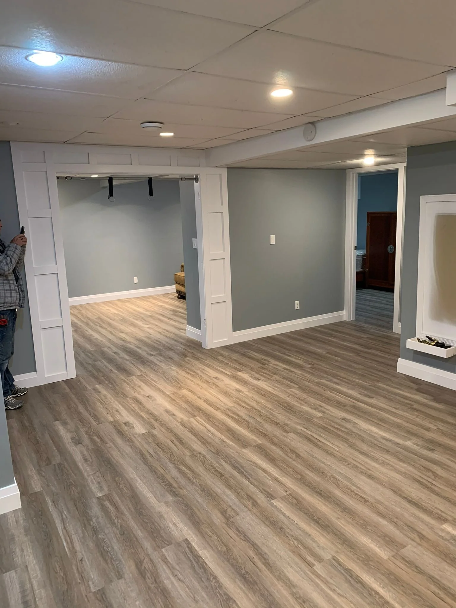 Room with wood-look flooring, blue-gray walls, white trim, ceiling lights, and doorways leading to other rooms.